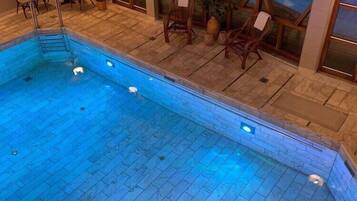 Ein überdachter Pool mit gefliestem Boden und einer Holzterrasse mit Stühlen und Tischen.