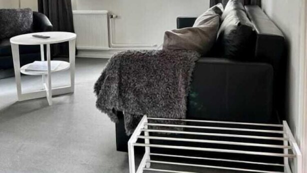 A modern living room with a black sofa, a white side table, and a drying rack. - Hotel Mullsjö (Mullsjö)