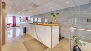 A hotel reception area with a marble counter, a glass railing, and a potted plant. - First Hotel Oxelösund (Oxelosund)