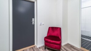 A room with a dark door, a red chair, and a tiled floor. - First Hotel Oxelösund (Oxelosund)