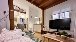 Una sala de estar acogedora con un televisor de pantalla plana grande, un sofá cómodo, una mesa de centro de madera y una planta pequeña.