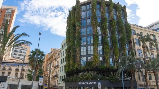 Un edificio con jardines verticales en la fachada, una tienda con letrero 'RISTORANTE' y palmeras cerca.