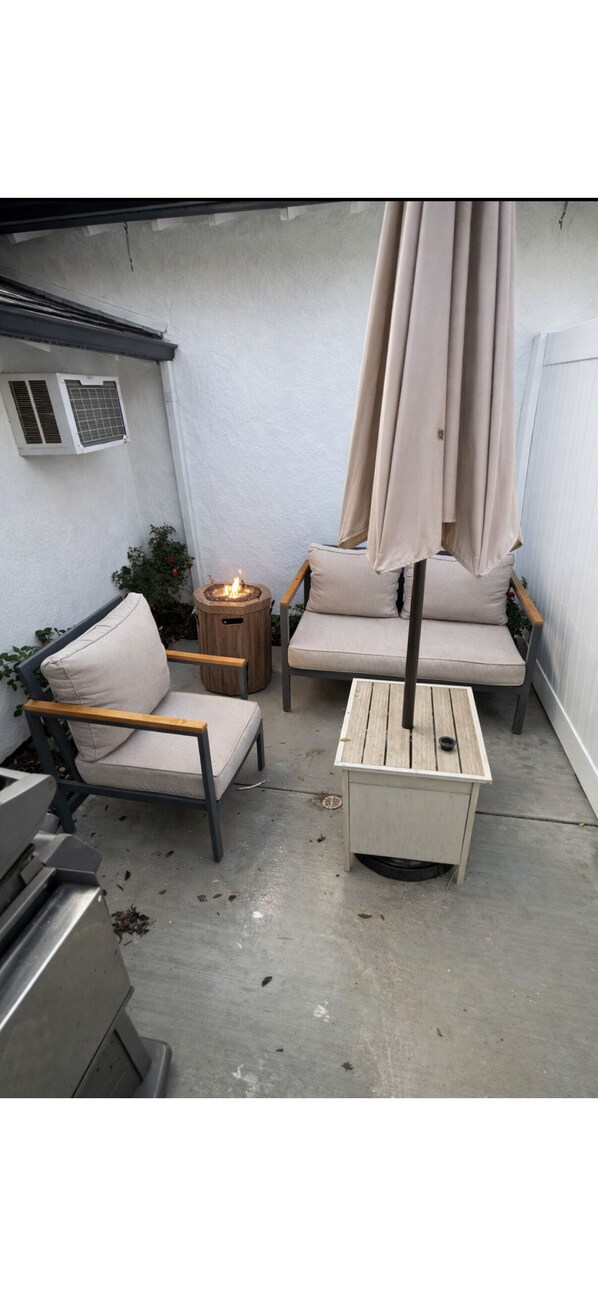 Un patio con dos sofás color beige, una mesita redonda con una vela y una mesa de madera con base metálica.
