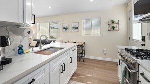 A modern kitchen with white cabinetry, a built-in stove, and a large island with a sink. - Luxury 1BR Suite Kitchen, Fireplace, Laundry, BBQ (Simi Valley)