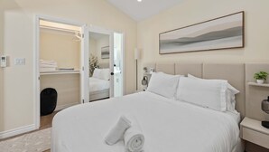A hotel room with a large bed, a walk-in closet, a bedside table with a lamp, and a painting on the wall. - Luxury 1BR Suite Kitchen, Fireplace, Laundry, BBQ (Simi Valley)