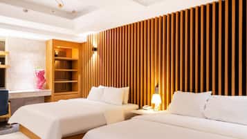 A hotel room with two beds, a wooden slat wall, a desk with a lamp, and a small seating area with a chair.