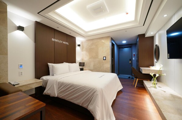 A hotel room with a large bed, a desk, a chair, a vanity with a mirror, and a wall-mounted TV. - Bentley Hotel Chungjang (Gwangju)