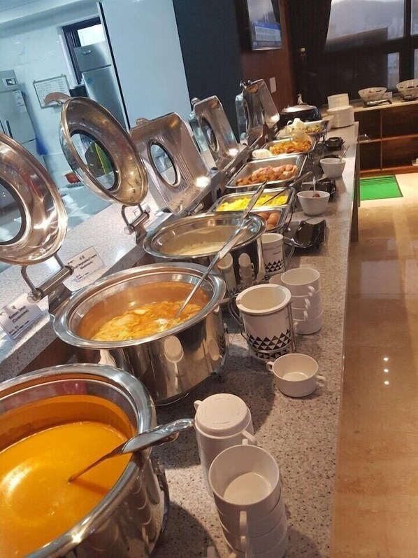 Una barra de buffet con varios recipientes de comida y utensilios para servir.