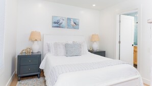 A bedroom with a large bed, two bedside tables with lamps, a nightstand, and two wall-mounted paintings of birds.