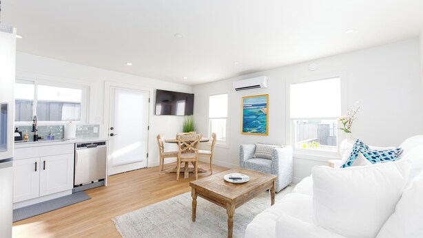 A modern living room with a white sofa, a wooden coffee table, and a dining area with a wooden table and chairs.