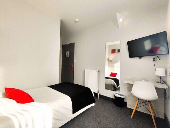 A hotel room with a bed, a desk, a chair, a TV, and a mirror. - Brit Hotel Suisse Et Bordeaux (Grenoble)