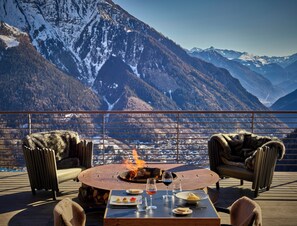 A dining area with a fire table, chairs, and a view of snow-capped mountains. - Le Massif Hotel & Lodge Courmayeur (Courmayeur)