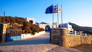 A hotel entrance with a stone wall, a blue gate, and a flag. - Amorgion Hotel (Amorgos)