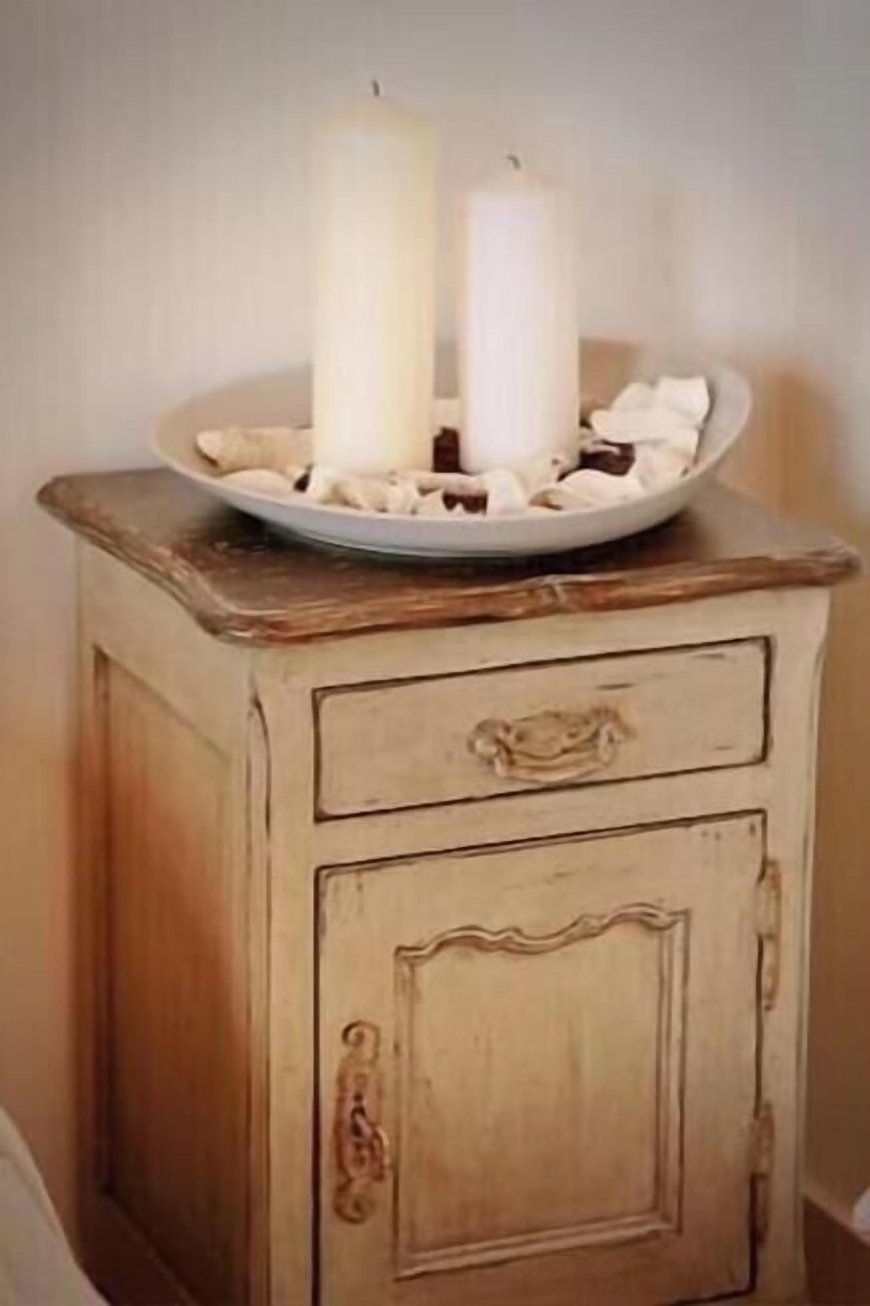 Un mueble de madera antiguo con dos velas blancas encima, un plato con fresas bañadas en chocolate y una vela blanca en un candelabro de vidrio.