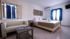 A hotel room with a bed, a sofa, a small table, and a painting on the wall. - Amorgion Hotel (Amorgos)
