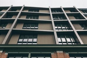 Un immeuble à étages dont la façade présente une structure en forme de grille, avec des fenêtres régulièrement espacées et une base en briques.
