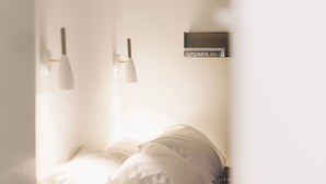 A hotel room with a bed, a bedside table, and a wall-mounted shelf with a book titled "The Upstarts" by Brad Stone. - Yust Antwerpen (Antwerp)