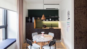 A compact kitchen with a round table and chairs, a hanging pendant light, and a view of the outside through a window. - Yust Antwerpen (Antwerp)
