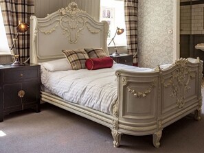 A classic bed with ornate headboard and footboard, a bedside table with a lamp, and a nightstand with a lamp. - The Dirty Bottles Inn (Alnwick)