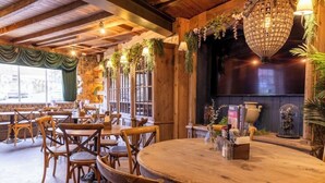 Un interior rústico con mesas y sillas de madera, una araña y plantas.
