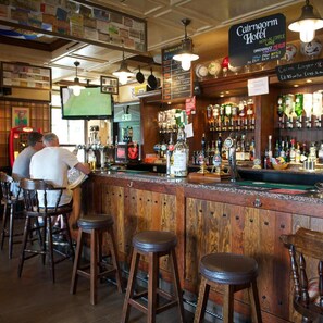 A bar area with wooden stools, a selection of bottles, and a menu board. - Cairngorm Hotel (Aviemore)