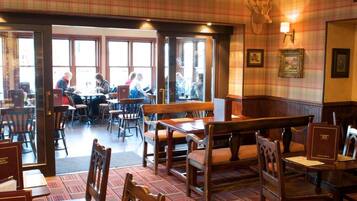 A restaurant interior with wooden tables and chairs, a patterned carpet, and a chandelier.