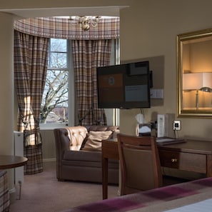 Ein Hotelzimmer mit einer Ledersofa, einem Schreibtisch mit Computer, einem großen Spiegel und karierten Vorhängen.