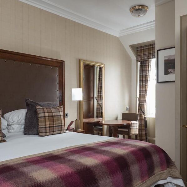 Habitación de hotel con cama, mesita de noche, silla, espejo y ventana con cortinas.