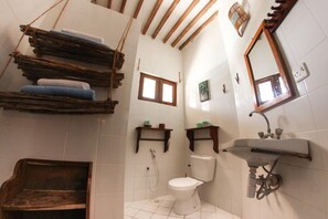 A bathroom with a toilet, sink, wooden shelves, and a window. - Kipepeo Lodge (Jambiani)