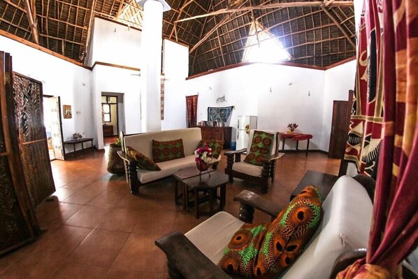 A spacious living area with a high ceiling and a rustic wooden structure. - Kipepeo Lodge (Jambiani)