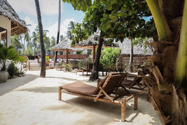 A beachside lounge area with wooden lounge chairs and thatched-roof structures. - Kipepeo Lodge (Jambiani)