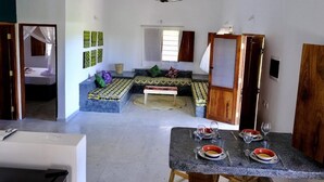 Habitació amb llit, taula de dinar preparada per a dues persones i una petita zona de seients amb coixins.