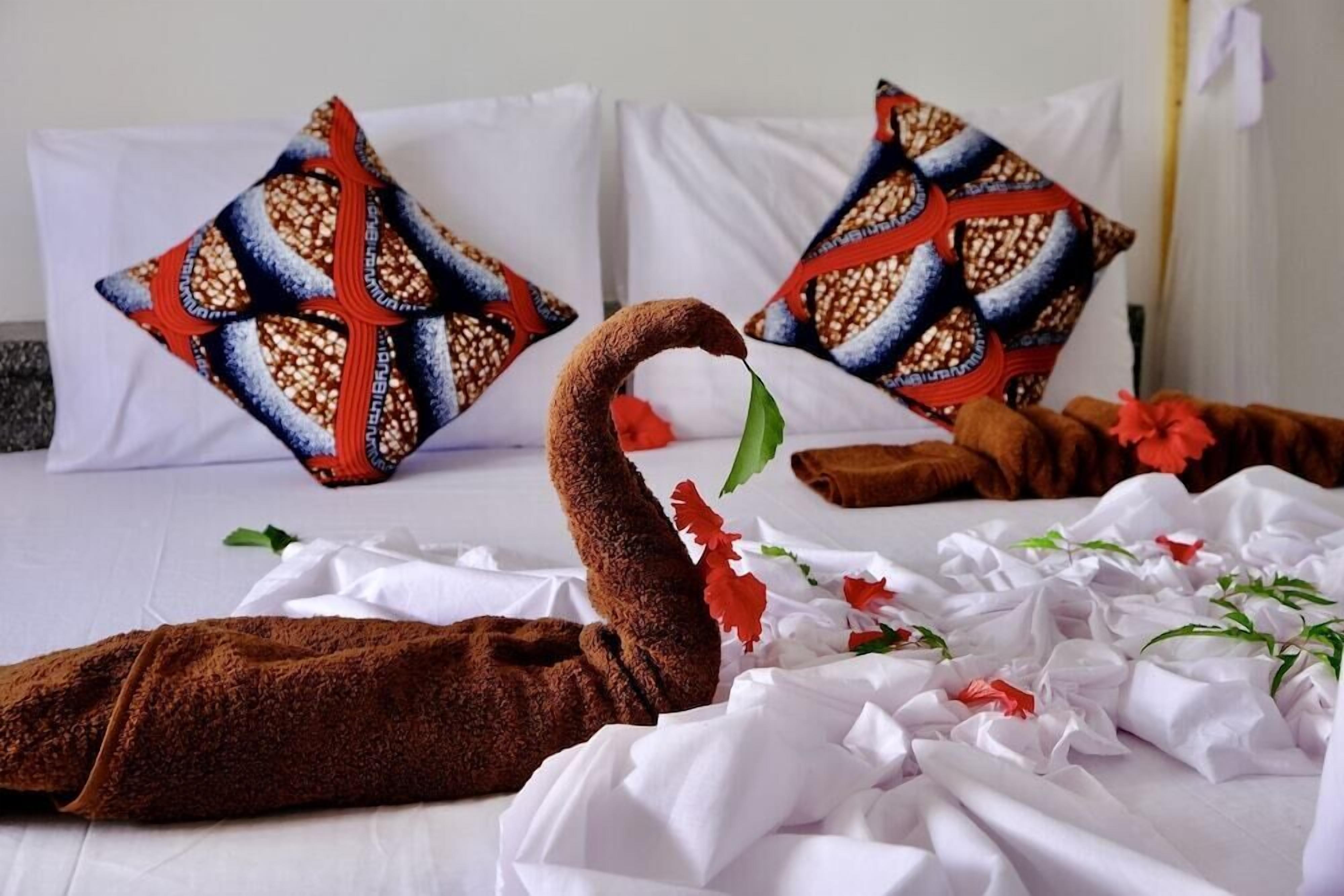 A hotel room with a neatly made bed, two patterned pillows, and a decorative swan head made of brown material.