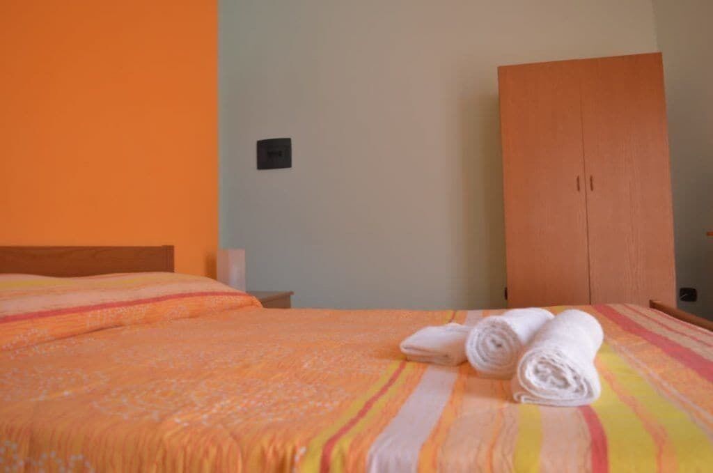 A hotel room with a bed, a wooden wardrobe, and a wall-mounted light switch.