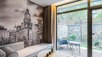 Een moderne woonkamer met een groot raam, een bank, een bijzettafeltje en een stadsgezicht muurschildering.