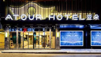 De buitenkant van het Atour Hotel, met verlichte borden, grote glazen ramen en een moderne gevel.