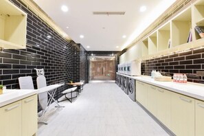 A modern laundry room with black and white tiled walls, a central washing machine area, and a seating area with a table and chairs. - Atour Hotel (Beijing)