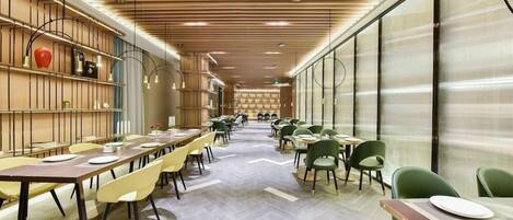 A modern dining area with long tables and chairs, wooden ceiling panels, and a herringbone floor pattern.