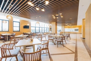 Un comedor amplio con mesas y sillas de madera, ventanas grandes y un diseño moderno en el techo.