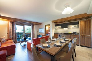 A dining area with a table set for four, a sofa, and a kitchen in the background. - MGM Hôtels et Résidences - Residence Alexane (Samoëns)