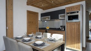 A modern kitchen with built-in appliances, a dining area with a wooden table set for four, and a wooden ceiling. - MGM Hôtels et Résidences - Residence Alexane (Samoëns)