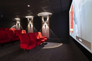 A movie theater with red seats, wall-mounted lights, and a large screen. - MGM Hôtels et Résidences - Residence Alexane (Samoëns)