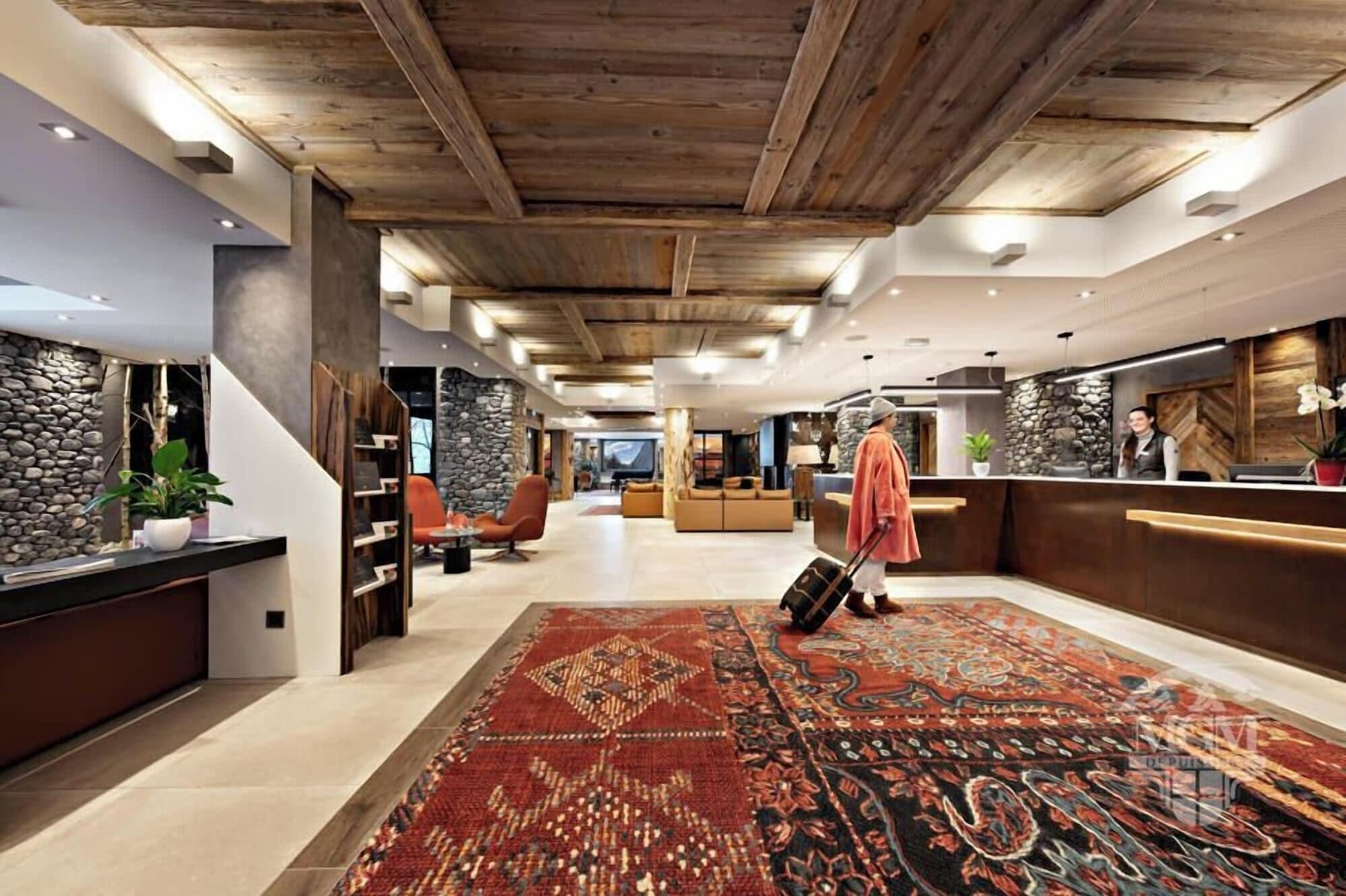 A hotel lobby with a wooden ceiling, a reception desk, seating area, and a patterned carpet.