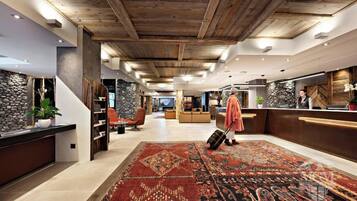 A hotel lobby with a wooden ceiling, a reception desk, seating area, and a patterned carpet.