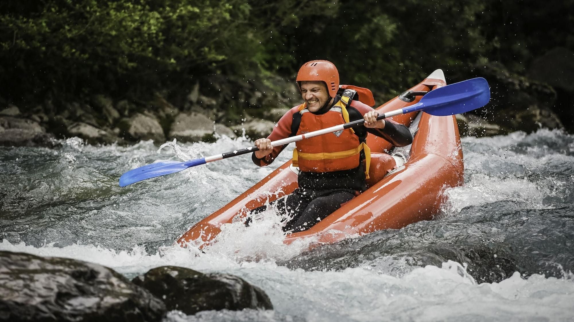 Une personne dans un kayak rouge navigue sur une rivière.