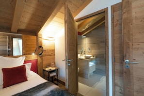 Un dormitorio con cama, almohada roja, mesita de noche y techo de madera.