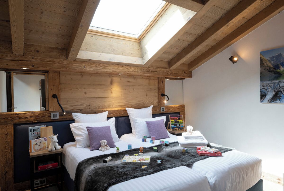 Ein Schlafzimmer mit Oberlicht, Holzbalken, einem Bett mit weißer Bettwäsche, einem Nachttisch mit Lampe und einer Wanduhr.