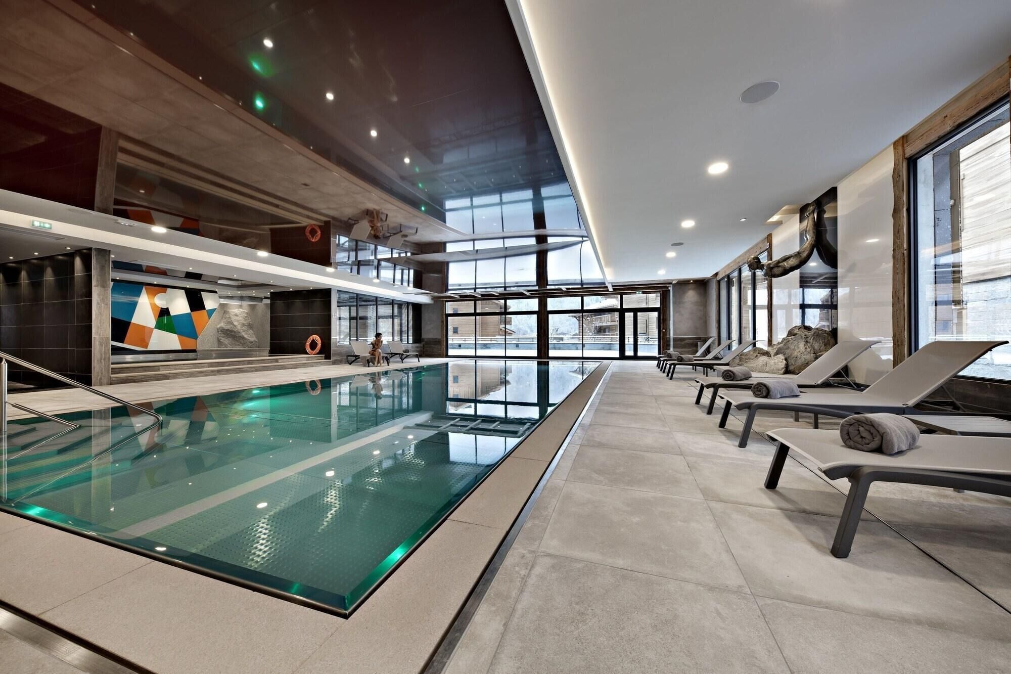 Piscina interior moderna con sillas de descanso y un amplio ventanal con vistas al exterior.