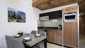 Una cocina moderna con armarios de madera, horno empotrado y comedor con mesa para dos.