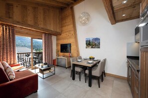 A modern interior with a dining area, kitchen, and a view of the outdoors. - MGM Hôtels et Résidences - Residence Alexane (Samoëns)